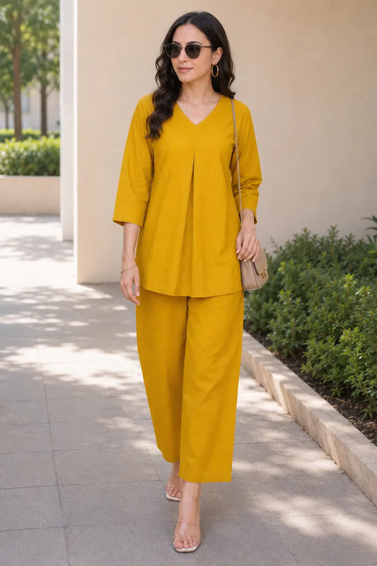 Rabric mustard yellow solid cotton casual co-ord set for women styled with sunglasses, featuring a V-neck top and wide-leg pajama.