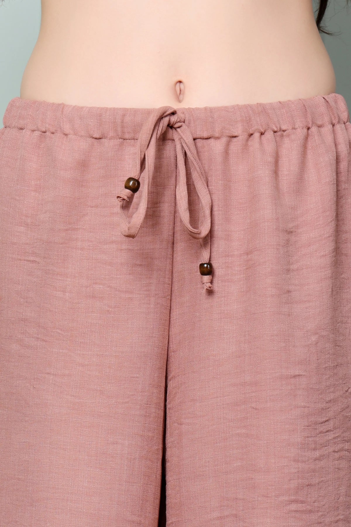 Close-up of RABRIC dusty rose linen trousers with adjustable drawstring and wooden ring detail
