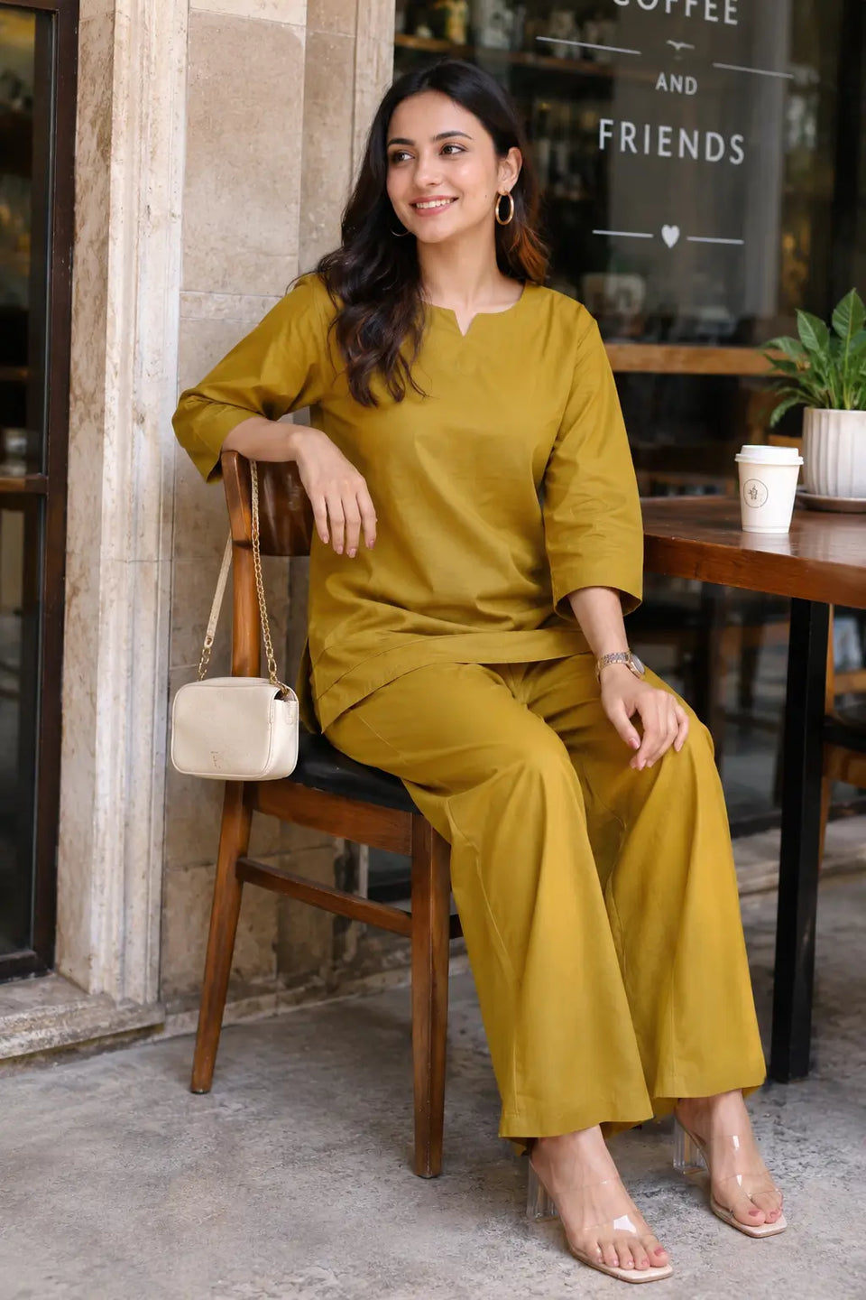 Rabric mustard olive cotton co-ord set for women in cafe sitting pose with notch neck top and matching wide leg pants