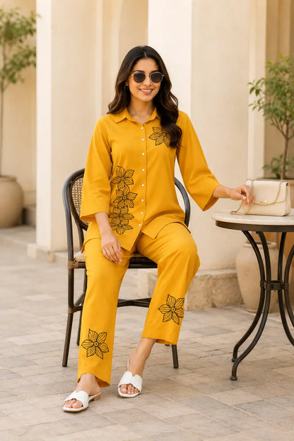 Sitting pose lifestyle image of Rabric mustard yellow rayon floral co-ord set for women with collared shirt and straight fit pants