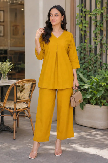 Woman wearing Rabric mustard yellow solid cotton co-ord set with plain V-neck short top, wide-leg pajama and casual sling bag outdoors.