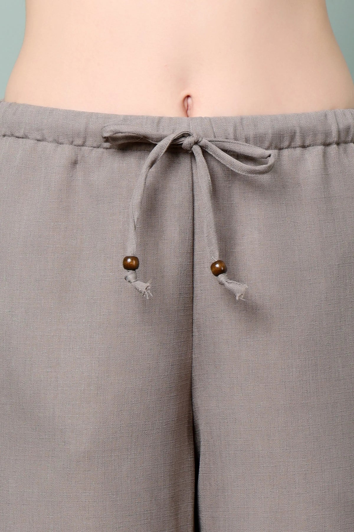 Close-up of RABRIC taupe linen trousers with adjustable drawstring and wooden bead detailing