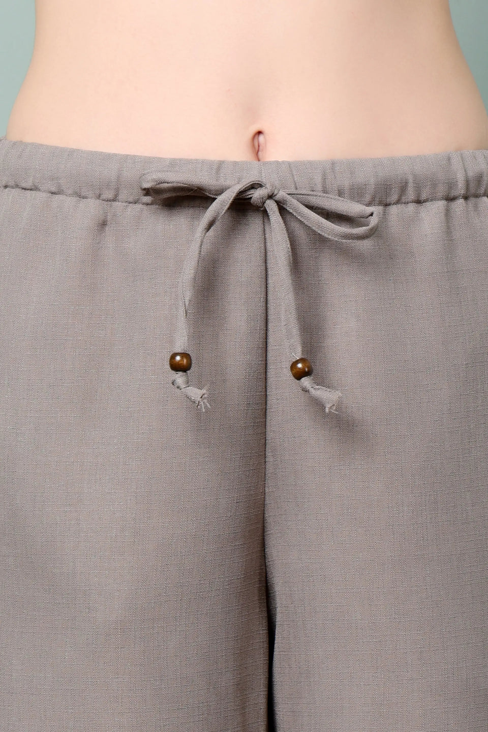 Close-up of RABRIC taupe linen trousers with adjustable drawstring and wooden bead detailing