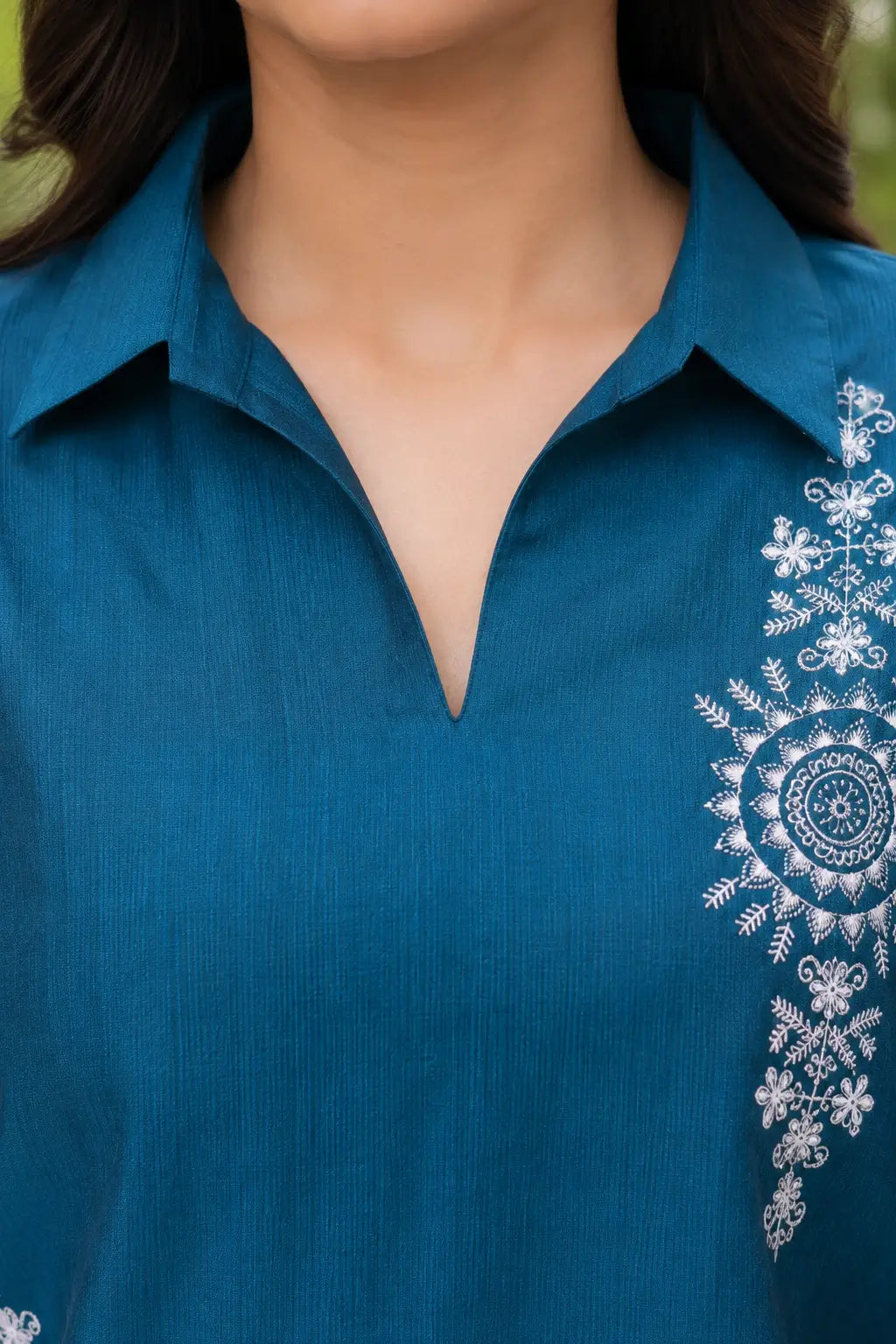 Close-up of Rabric teal blue Vertican silk co-ord set featuring stylish collar V-neck design with intricate white floral embroidery and premium fabric texture.