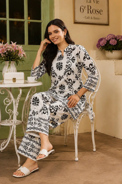 Rabric white Vertican Silk black damask print co-ord set shown in casual sitting pose with handbag and cafe accessories.