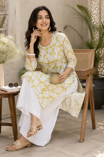 Lifestyle image of woman sitting in yellow white floral cotton kurti with casual accessories and white palazzo by Rabric